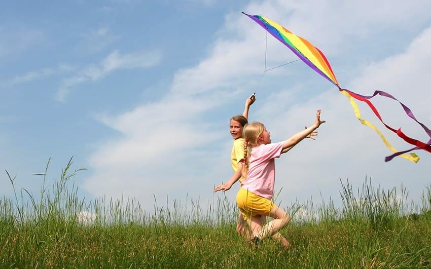 two girls outside in grass flying a kite