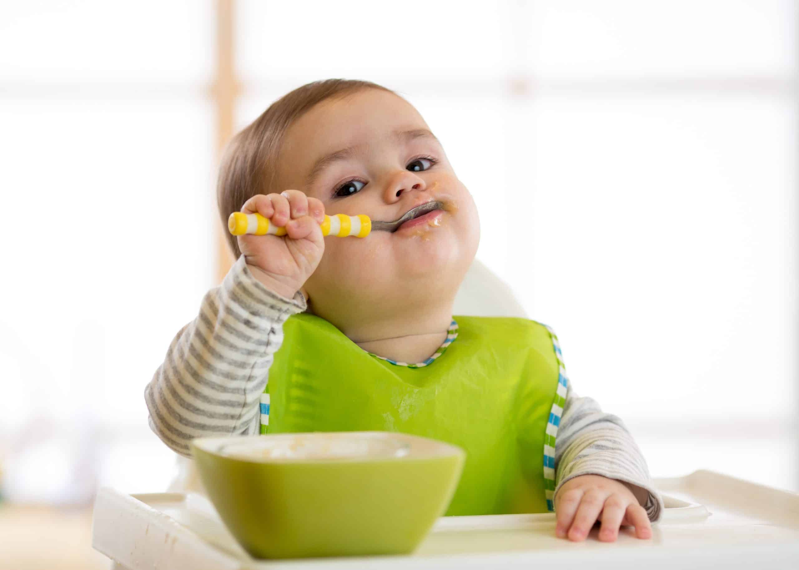 Baby feeding himself with a spoon eating out of a bowl