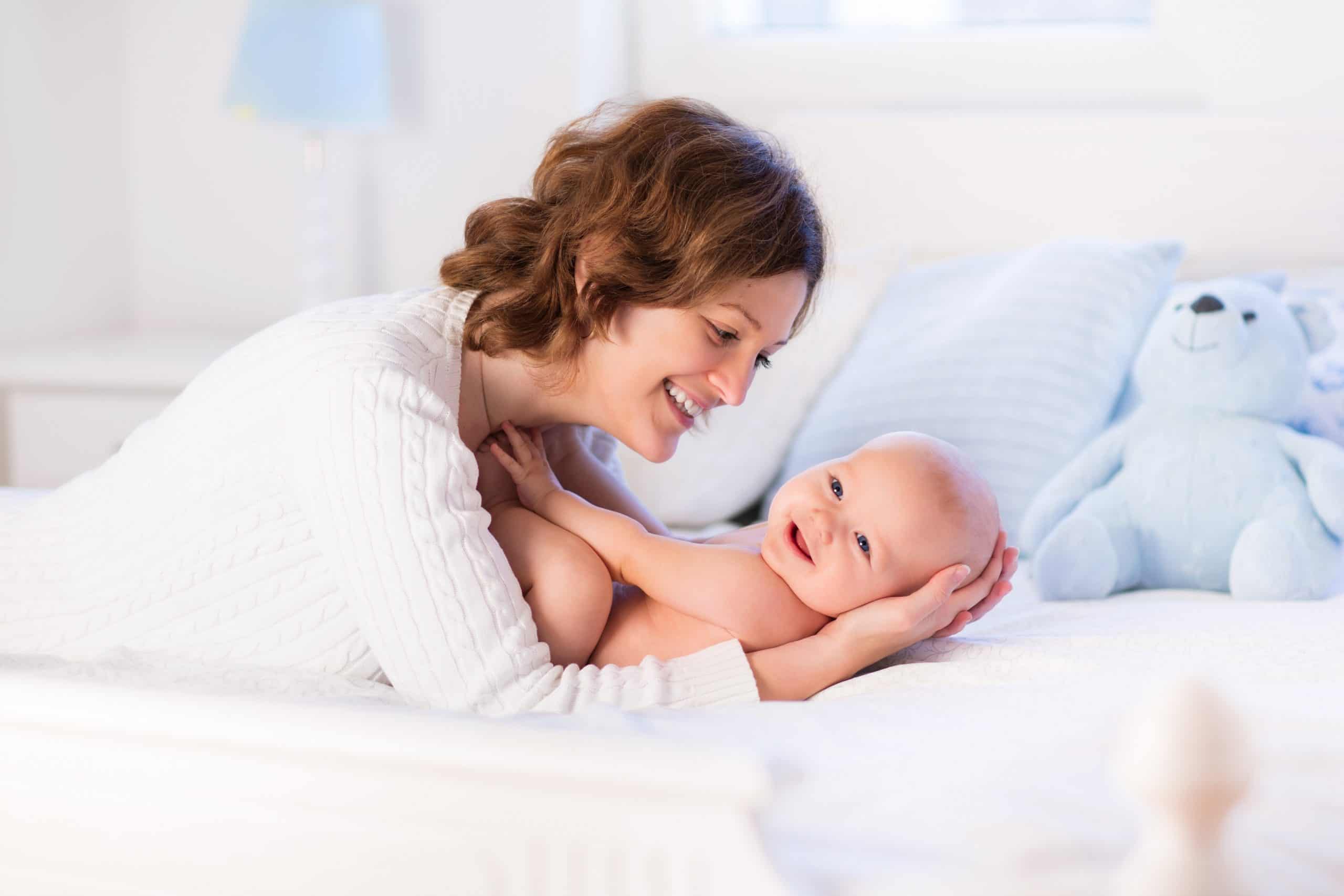 Mother and baby on a white bed Mother holding smiling baby on bed