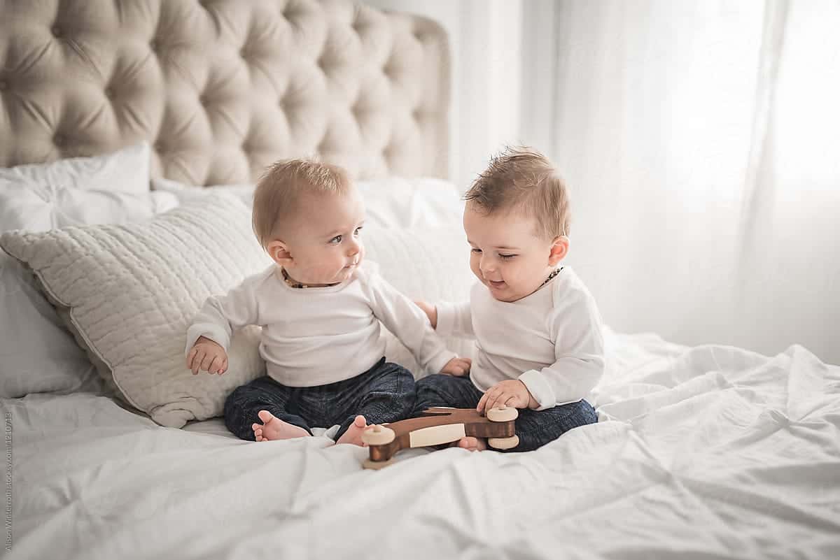 Twin infants playing with a toy together on a bed