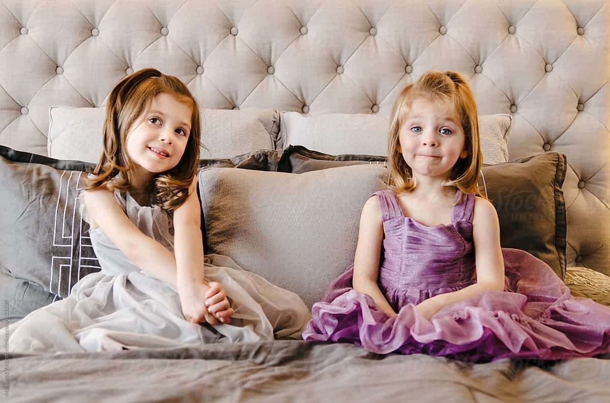 Two little girls in dresses sitting on a bed – job Two little girls in dresses sitting on a bed