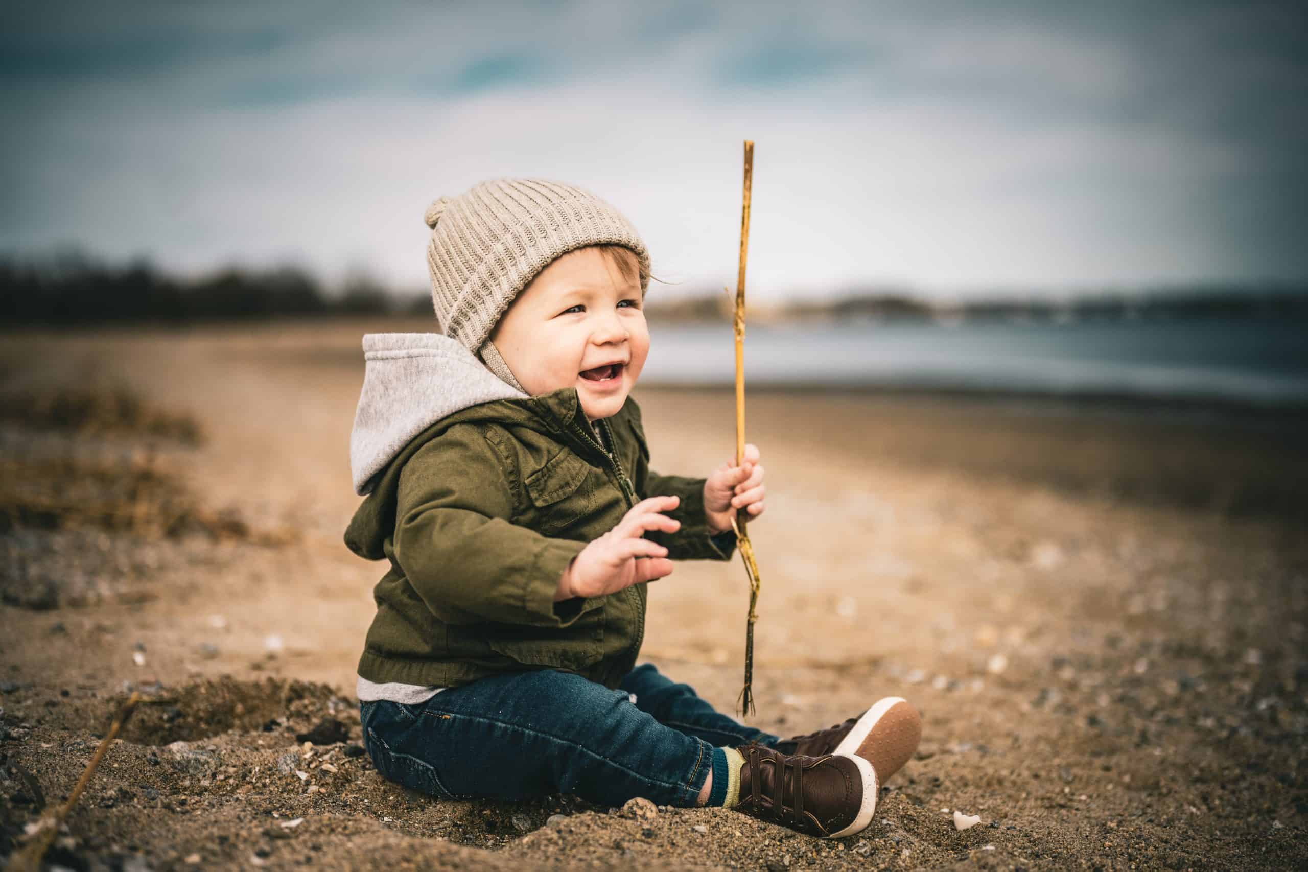 Little boy bundled up at the beach – job Little boy bundled up and holding a stick at the beach