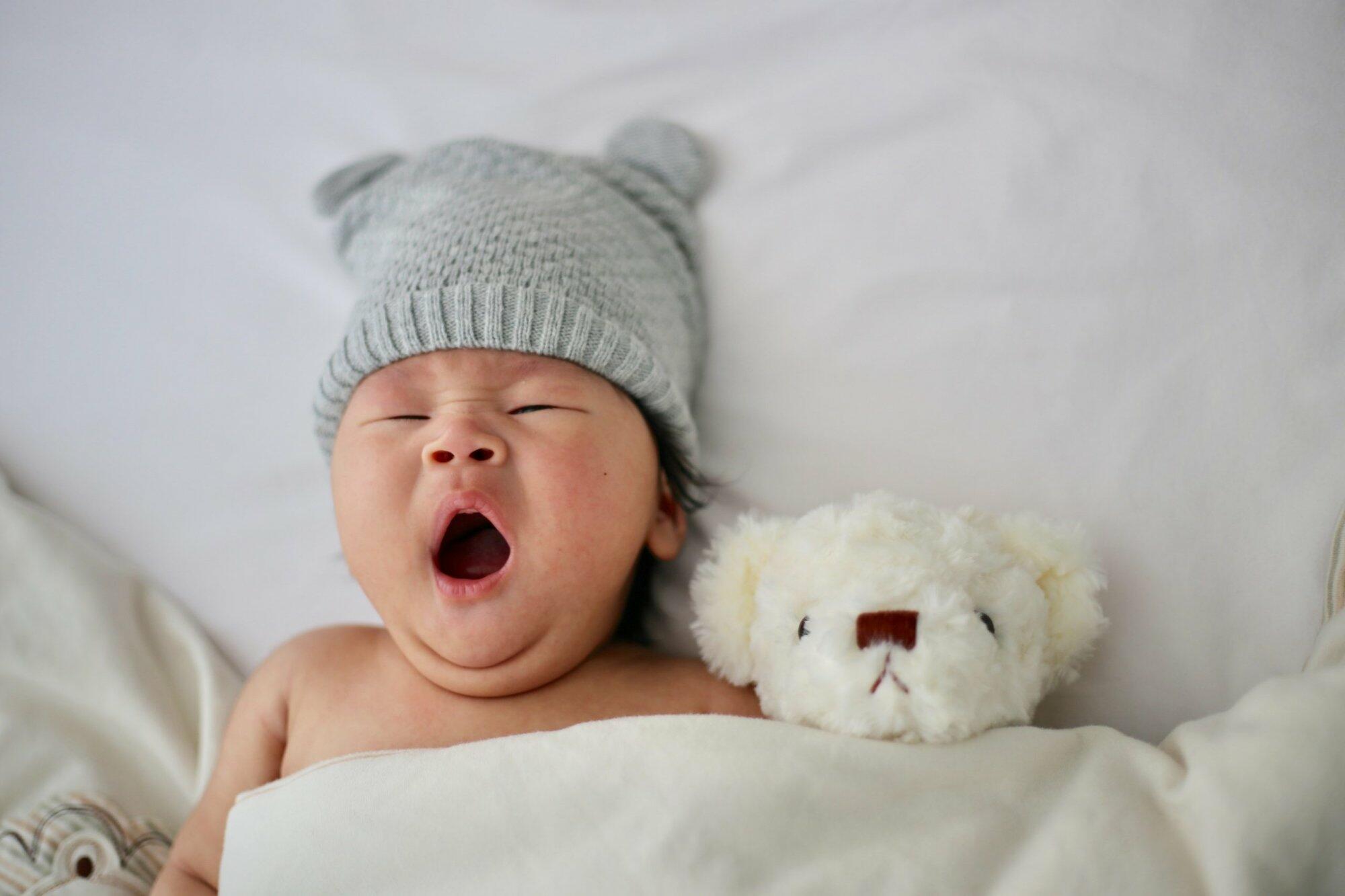 Newborn baby yawning in a crib with a stuffed bear